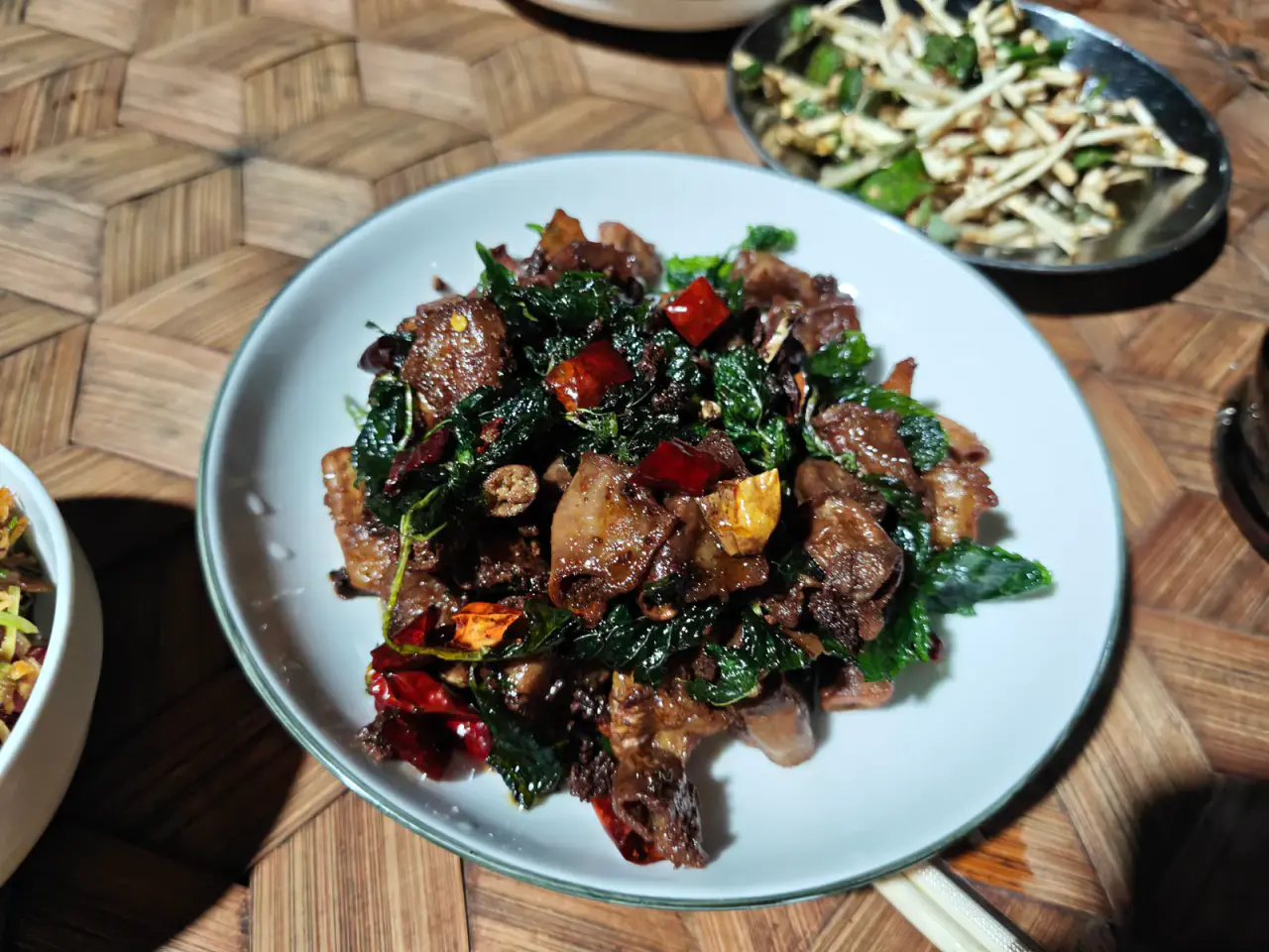 A plate of pork, herbs and dried chillies on a woven table during dinner in the Bulang Mountain area